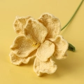 Macro shot of handmade yellow crochet eustoma flower with green leaves on yellow background - Yellow