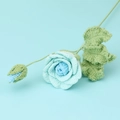 Nahaufnahme einer handgefertigten Häkelrose in Blau mit grünen Blättern und Stiel - Verlauf Blau (Rosenzweig)