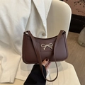 Bolso de hombro marrón oscuro de moda con lazo dorado sobre una silla blanca - Marrón