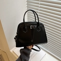 Elegante bolso trapezoidal negro con detalles plateados y doble asa sobre un alféizar luminoso - Negro