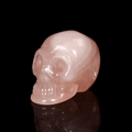Polished natural rose quartz crystal skull carving displayed on a reflective black background - 2 Inch / Rose Quartz