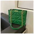 Green quilted tote bag with geometric pattern and gold chain strap on a black sofa - Green