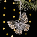 Adorno navideño de mariposa transparente con lentejuelas doradas en una rama de pino - Estilo Mariposa Transparente con Lentejuelas