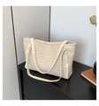 Close-up of beige woven straw tote bag with smooth shoulder strap on black surface - Off White