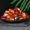 Polished red agate tumbled stones in a black tray with tropical green leaf decor - 100 Grams Of Red Agate 1-2 Cm In Size.