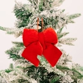 Vibrant red velvet Christmas bow ornament hanging on a snowy pine tree branch - Small / Red