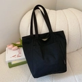 Minimalist black canvas tote bag with front pocket and white fashion label on sofa - Black