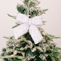 Sparkling white sequined Christmas bow ornament hanging on a snowy festive tree branch - Small White
