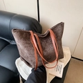 Bolso tote grande de tejido café con asas de cuero naranja sobre un sofá negro - Marrón