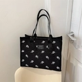 Borsa tote in tela nera con stampa a rose bianche posizionata su una sedia minimalista - Nero