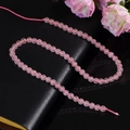 Filo di perle di quarzo rosa da 6 mm a forma di S su elegante sfondo di pelle nera - Quarzo Rosa Premium