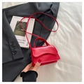 Detail of red square crossbody bag with wavy flap design on white fabric and black suit - Red