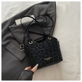 Detailaufnahme der Leoparden-Beuteltasche mit Goldlogo auf grauem Blazer-Hintergrund - Schwarzer Leopard