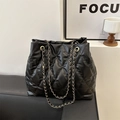 Modern black quilted bucket tote bag with gold chain straps on a stylish black sofa - Black