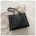 Dettaglio borsa tote in pelle nera con borchie dorate e texture a grana su completo - Nero
