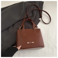 Detail of a brown leather fashion handbag with a metal rivet and FASHION logo - Dark Brown