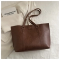 Detail of dark brown leather tote bag with gold logo text and vertical seam stitching - Brown