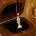 Macro detail of a colorful enamel fish pendant with ruby eye on a gold chain necklace - Blue Yellow Fish