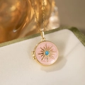 Macro view of a vintage round pink enamel locket necklace with gold sunburst and blue bead - Round Sun Locket / Pink