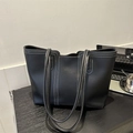 Large black tote bag with white contrast stitching and slim handles on wooden table - Black