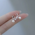 Detail of silver bow earrings with square zircon and hanging white pearl on fingertips - Cross Zirconia Pearl-Silver