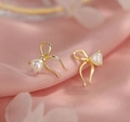 Detail of elegant gold bow earrings with heart-shaped pearls on soft pink silk fabric - Gold Heart Pearl Bow Stud Earrings