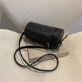 Retro black leather cylinder bag with metal zipper and thin strap on a book - Black