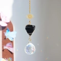 Detail of suncatcher with sun metal charm, black raw stone, and crystal ball reflecting light - 35cm / Obsidian