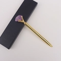 Nahaufnahme des goldenen Kugelschreibers mit lila Rohkristall und schwarzer Geschenkbox - Amethyst