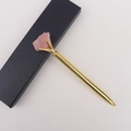 Detail eines Rosenquarz-Rohsteins auf goldenem Kugelschreiber mit schwarzer Box - Rosenquarz