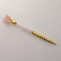 Dettaglio di una penna in metallo dorato con un grande cristallo rosa grezzo - Quarzo rosa