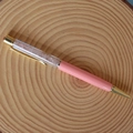 Dettaglio di una penna a sfera in cristallo rosa con finiture dorate su fondo di legno - Quarzo rosa