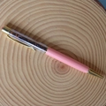 Dettaglio di penna a sfera rosa con cristalli e finiture dorate su sfondo in legno - Bracciale in pietra occhio di tigre