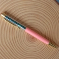 Detail of pink ballpoint pen with transparent barrel filled with green crystal gravel stones - Malachite