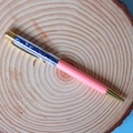 Dettaglio di una penna a sfera in cristallo rosa con accenti dorati su base di legno - Lapislazzuli