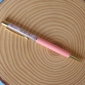 Macro detail of a pink crystal ballpoint pen with gold metal accents on a wooden stand - Kunzite