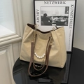 Elegante borsa tote beige con tracolla in pelle, catena dorata e perle su un tavolo nero - Cachi