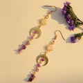 Detalle de pendientes celestiales dorados con dijes de sol luna y borlas de amatista - Amatista