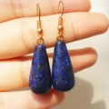 Dettaglio degli orecchini a goccia in cristallo blu con ganci a spirale dorati in mano - Lapislazzuli