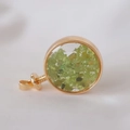Macro shot of gold-framed round crystal pendant with green stone chips on white knit - Peridot / 29mm