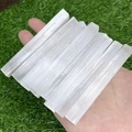 Natural white selenite crystal wands with fibrous texture held over green grass - White Selenite Stick