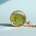 Portachiavi dorato tondo con fiala trasparente riempita di pietre di cristallo verde oliva - Peridoto