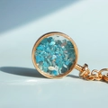 Portachiavi tondo in metallo dorato con ciondolo in vetro pieno di pietre di cristallo blu - Apatite