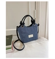 Detalle del bolso denim azul con asas de cuero y etiqueta de tela sobre un sofá blanco - Negro