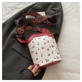 Close-up of cherry print bucket bag with colorful geometric strap and gold hardware - Red