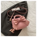 Detailed view of pink bow handbag with gold metal hardware on top of a blazer - Pink