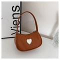 Detail of brown crescent shoulder bag with white heart and gold bow accent on white table - Brown