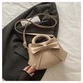 Detail of beige bow tote bag with golden hardware on a black blazer backdrop - Dark Khaki