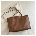 Detailansicht einer braunen Shopper-Tasche aus Leder auf weißem Blazer und Hintergrund - Braun