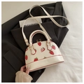 Detailansicht der weißen Muscheltasche mit Erdbeerdruck und goldener Hardware auf Jacke - Weiß